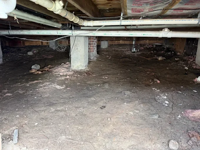 Crawl space under house with concrete floor, support columns, and HVAC piping after pest remediation