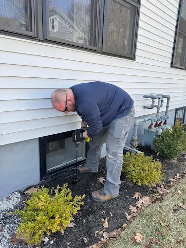 Technician applying pest control treatment to home foundation and basement window area