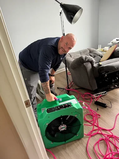 Technician operating green industrial air mover with pink cord on hardwood floor