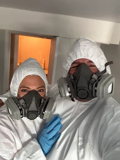 Two technicians in white hazmat suits and respirators preparing for pest control treatment