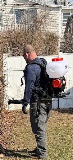 Technician using red and white motorized backpack sprayer for pest control treatment